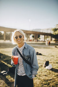 Portrait of smiling young man having drink while standing on lawn at concert