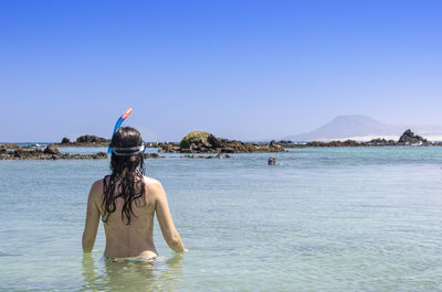 Rear view of woman standing on beach against clear sky