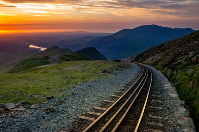 Railroad tracks leading towards mountains against sky