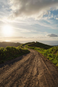 Dirt road amidst field against sky