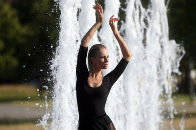 Beautiful woman with hand raised standing against fountain