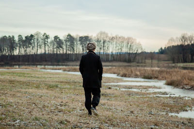 Rear view of man standing on field against sky