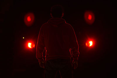 Rear view of man standing against illuminated lights at night