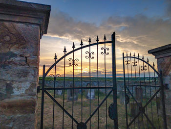 Metal fence against sky during sunset