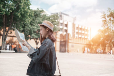 Side view of young woman using mobile phone in city