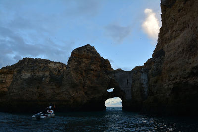 People on rock by sea against sky