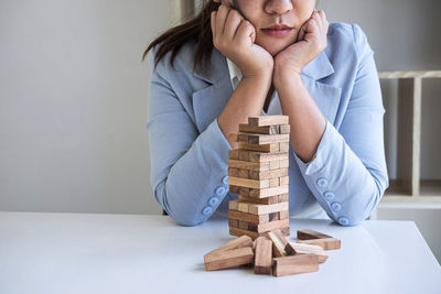 Midsection of businesswoman sitting by toy blocks on table against wall