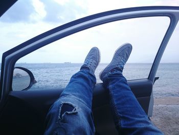 Low section of man relaxing in car at beach