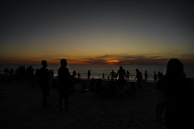 Silhouette people on beach against sky during sunset