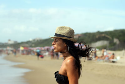 Side view of woman with eyes closed wearing hat standing at beach