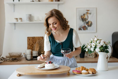 Beautiful girl adds a berry to the cake in the kitchen