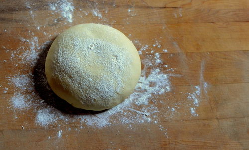 High angle view of pizza dough with flour on cutting board