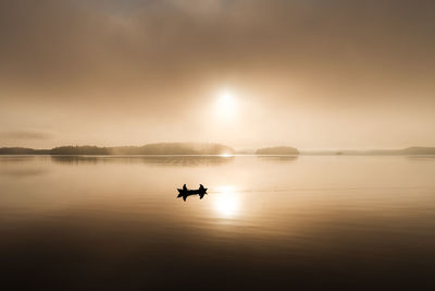 Silhouette man on boat in lake against sky during sunset