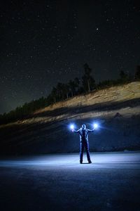 Man standing by illuminated light against sky at night