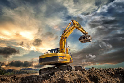 Earth mover at construction site against sky during sunset