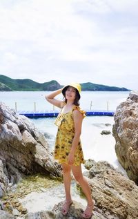 Woman standing on rock at beach against sky