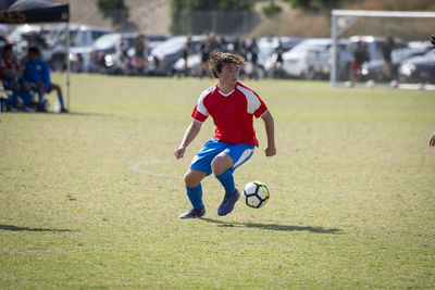 Teen soccer player in red and blue uniform controlling the ball during a game