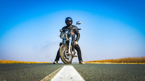 Man riding bicycle on road against clear blue sky