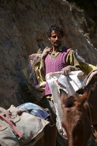 Man carrying sacks while walking with donkey by rock formation