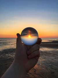 Cropped hand holding crystal ball at beach during sunset