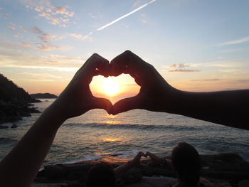 Close-up of hand holding heart shape against sky during sunset