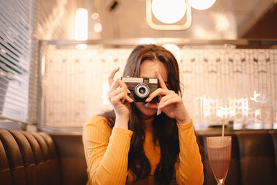 Teenage girl photographing with vintage camera while sitting in cafe
