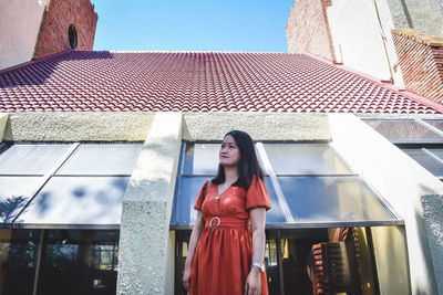 Portrait of young woman standing against building