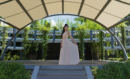 Beautiful woman in gown standing below arch built structure at park