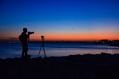 Silhouette man photographing at beach against sky during sunset