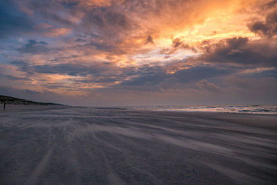Scenic view of beach against dramatic sky during sunset