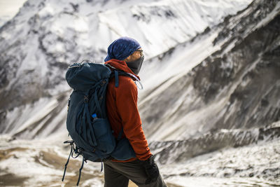 Side view of male hiker in warm outerwear standing on hill on background of snowy himalayas mountains in winter in nepal