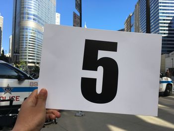 Low angle view of hand holding sign against sky in city