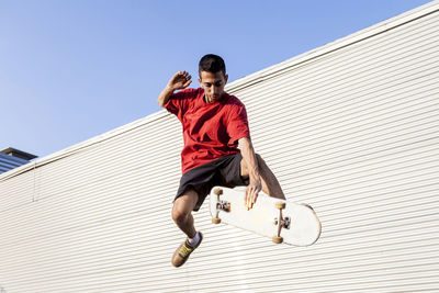Man with skateboard in mid-air against wall