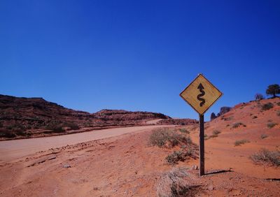 Road sign on landscape against clear blue sky