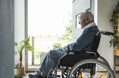 Senior man sitting in wheelchair by window at home