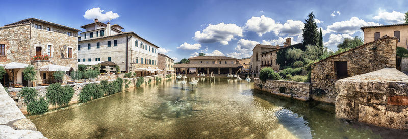 Buildings by canal against sky in city