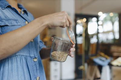 Midsection of female owner opening food jar while standing in cafe