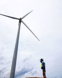 Low angle view of woman standing against windmill with sky in background