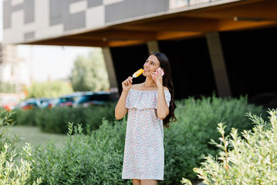 A charming girl is talking on the phone and eating ice cream while walking around the city