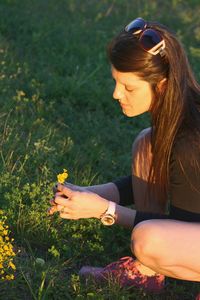 High angle view of woman plucking flowers while crouching on field