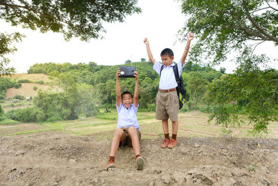 Excited students with radio on field against sky