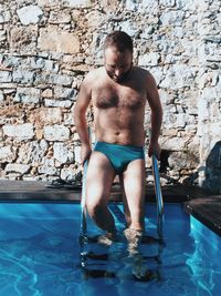 Full length of shirtless man in swimming pool against wall