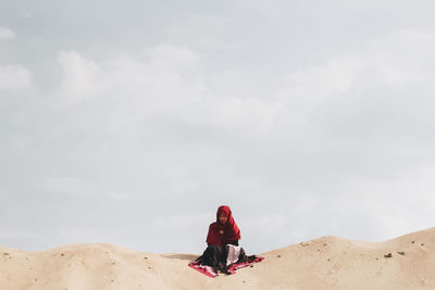 Woman sitting on sand against sky