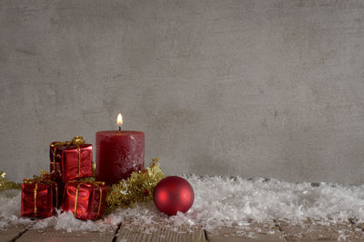 Lit candles with christmas ornaments and gifts on table against wall