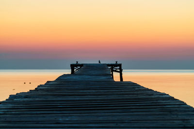 Pier over sea against orange sky