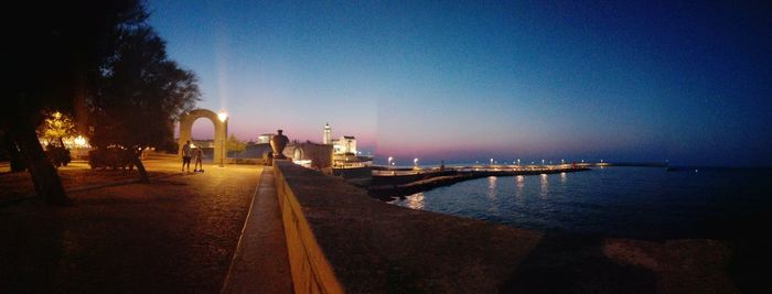 People on illuminated shore against clear sky at night