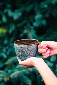 Female hand holding earthen cup with herbal tea with green natural background