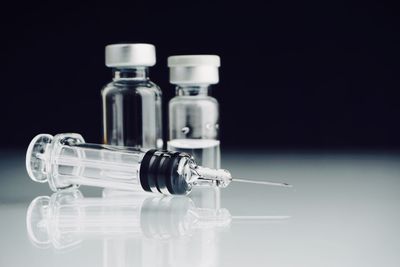 Close-up of syringe by vial bottles on table against black background