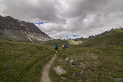 People walking on dirt road against cloudy sky