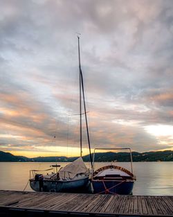 Sailboats moored in sea against sky during sunset